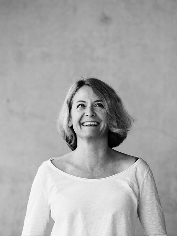 Schwarzweißporträt einer Frau mit kurzem blondem Haar, die ein weißes Hemd trägt und lächelt.