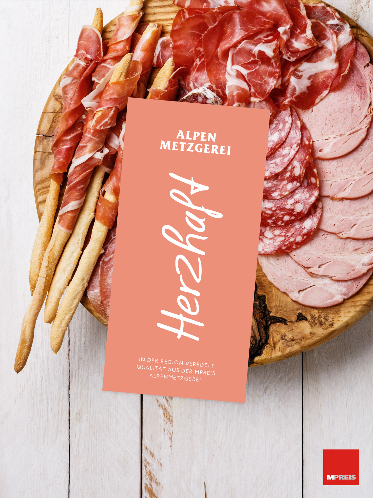 Wurstwaren auf Holzbrett, Alpen Metzgerei Karte mit Text "Herzhaft" und "In der Region veredelt. Qualität aus der MPreis Alpenmetzgerei".