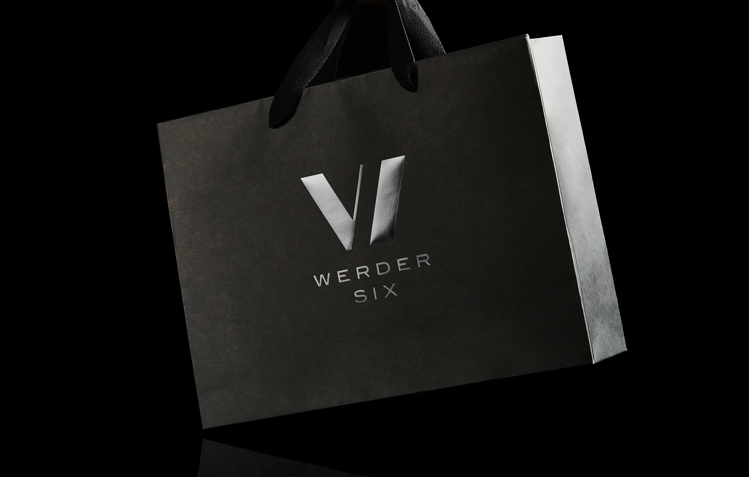 Eine schwarze Papiertüte mit dem silbernen Logo „VI WERDER SIX“ auf schwarzem Hintergrund.